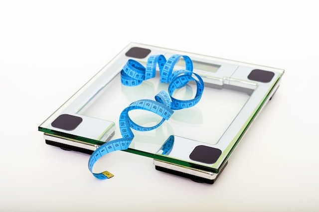 Square glass weighing scales with a blue measuring tape.