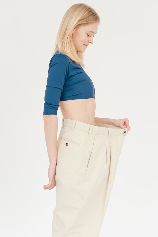 A blond woman in extra loose pants, signaling how much weight loss she has achieved.