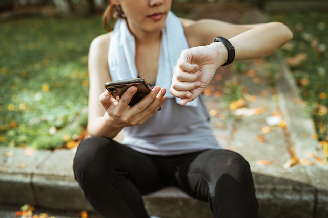 A woman in sports attire, sitting down and checking on her smartwatch.