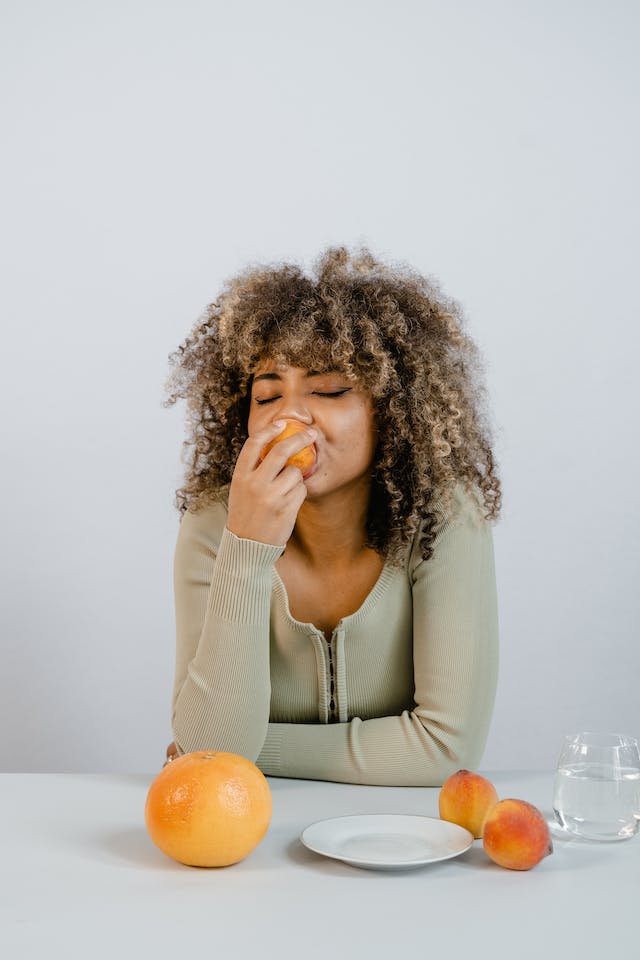 A curly-haired woman eating a piece of peach.