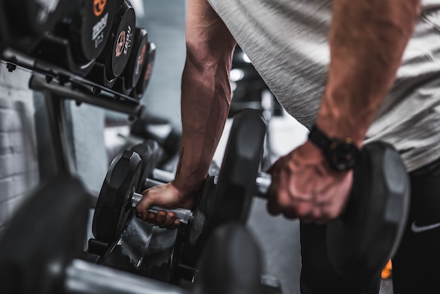 A man in a grey shirt holding a black dumbbell in each hand