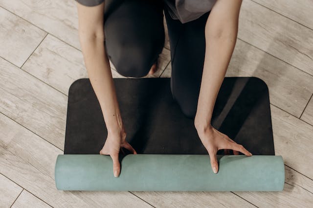 A woman unrolling her yoga mat on a wooden floor