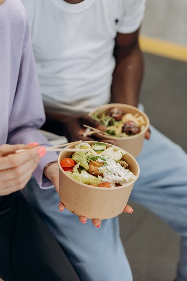Two people eating a bowl of healthy meal with chopsticks.