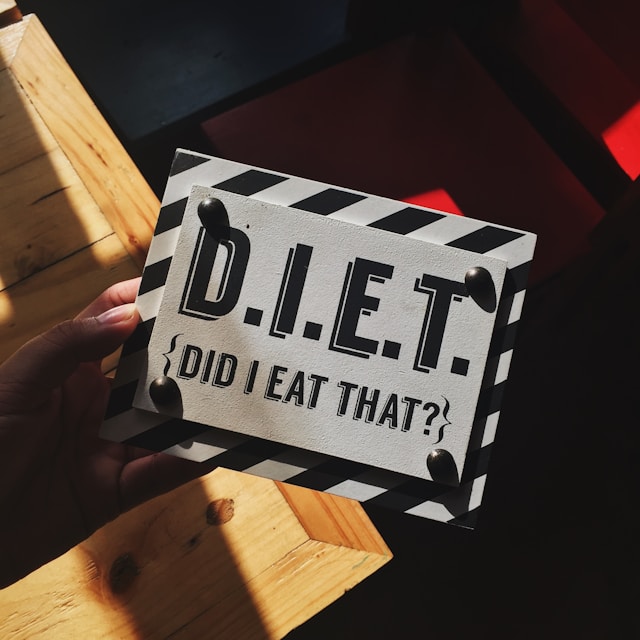 A person holding a striped border sign that reads "D.I.E.T." with the phrase "Did I Eat That?" written underneath.