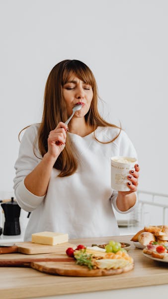 A woman enjoying a spoonful of ice cream with her eyes closed, savoring the taste, with more food in front of her.